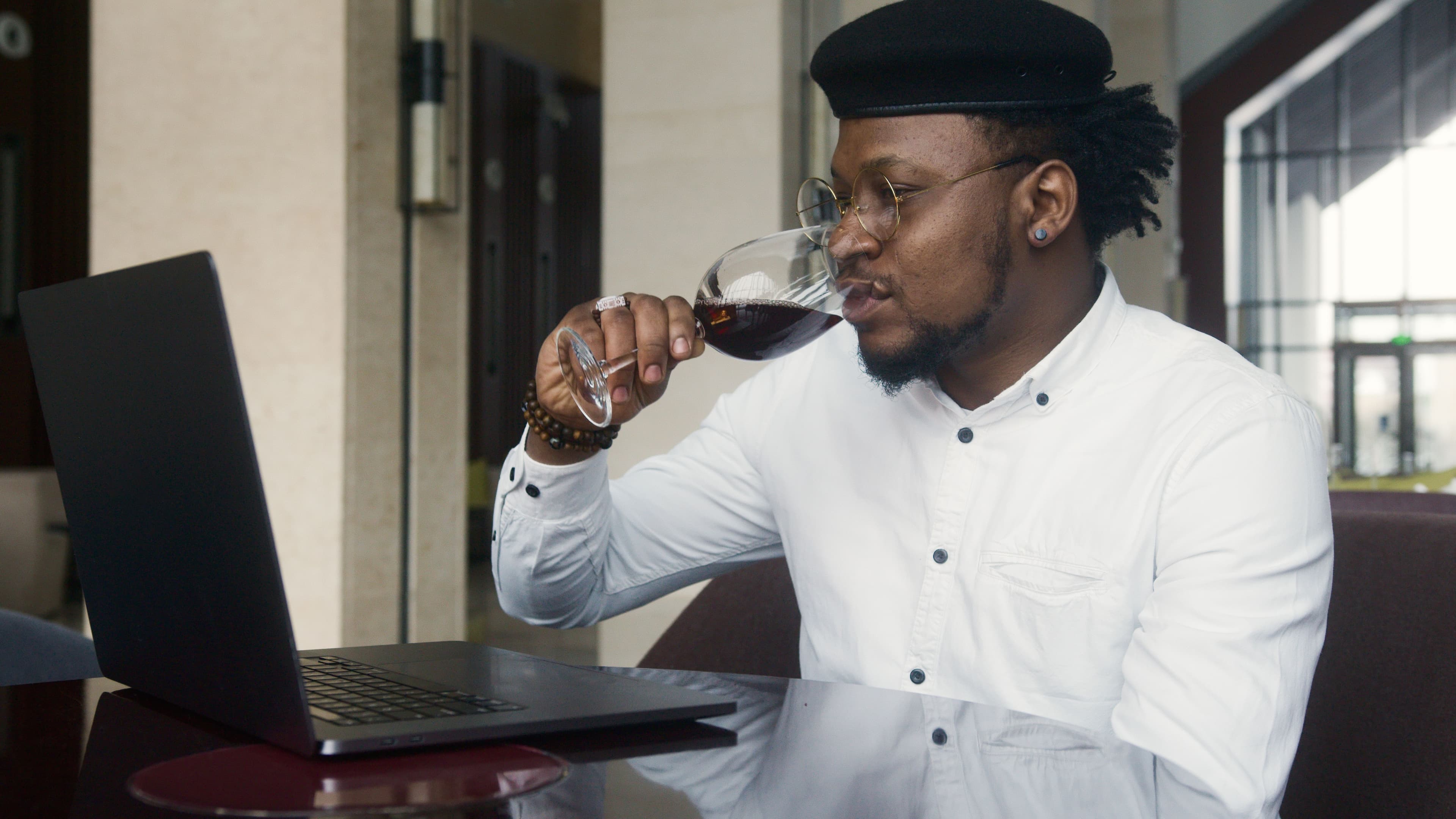 A wine rep checking a glass of wine at a laptop while prepping for a buyer meeting